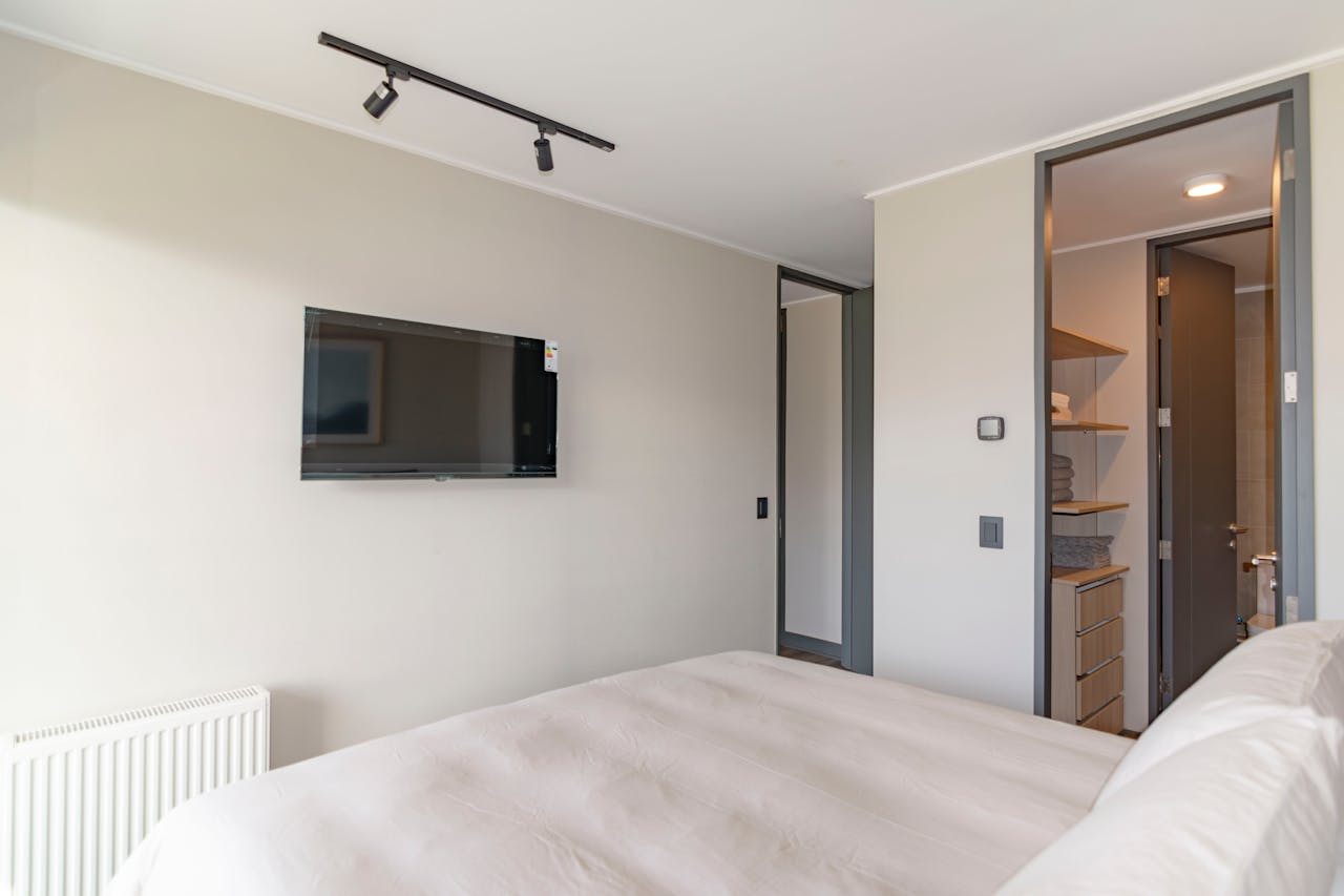 A modern bedroom featuring a cozy bed, wall-mounted TV, and minimalist decor.